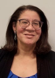 Karen Epps with eyeglasses wearing a black cardigan and blue blouse in front of white wall.