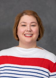 Smiling woman wearing white sweater with wide red and blue stripes.